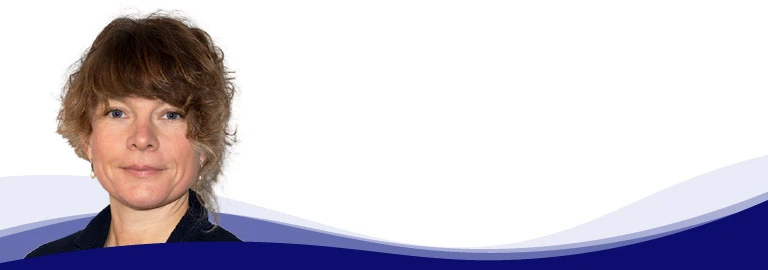 Sabrina Haas, responsible for Marketing Services at CREATON, looks calmly into the camera and smiles slightly. She has medium-length, curly, light brown hair with bangs. She is wearing a dark blouse and gold earrings.