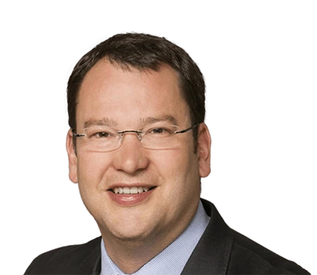 Dirk Amann, CTO Managing Director chez i.safe MOBILE, regarde la caméra en souriant. Il porte des lunettes sans monture, une chemise bleu clair et une veste sombre. Il a les cheveux courts, châtain foncé et un teint naturel.