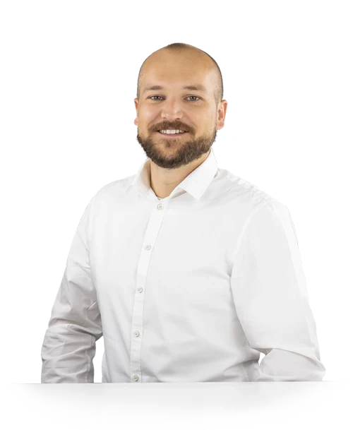 Michael Binder se tient derrière une table, vêtu d'une chemise blanche, et regarde la caméra en souriant.